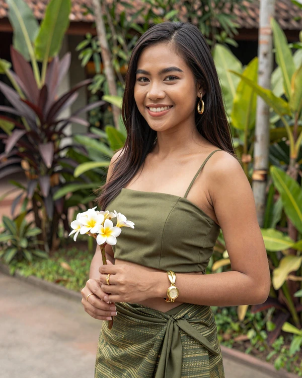 Laotian woman holding frangipani flowers in a lush tropical garden - Lao dating culture emphasizes gentle warmth and natural beauty
