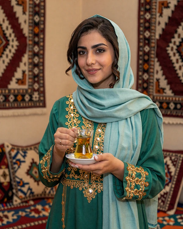 Afghan woman in traditional embroidered dress drinking cardamom tea in a warmly decorated room - explore Afghan dating culture on our platform